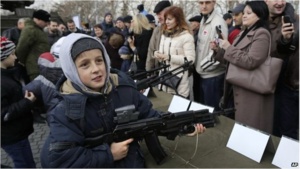 A child in Sevastopol plays with a weapon displayed as part of a promotional campaign by the Russian Army. Source: BBC News.